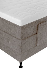 Close-up vanuit schuin bovenaanzicht van een beige gestoffeerd boxspringbed met een wit, golvend doorgestikt topmatras en zwarte poot.