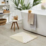 Badteppich Leandra in Beige mit weißem geometrischem Muster auf einem Badezimmerboden, im Vordergrund aus der Vogelperspektive fotografiert.