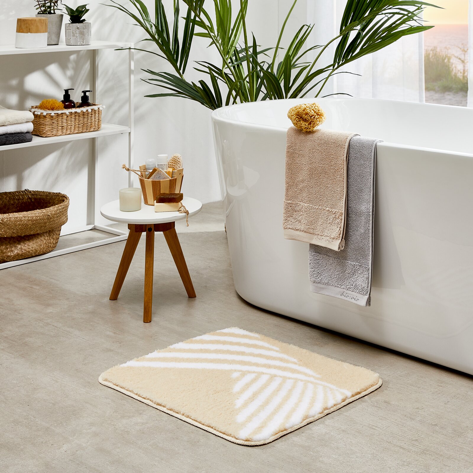 Badkamertapijt Leandra in beige met een wit geometrisch patroon op een badkamervloer, gefotografeerd vanuit vogelperspectief op de voorgrond.