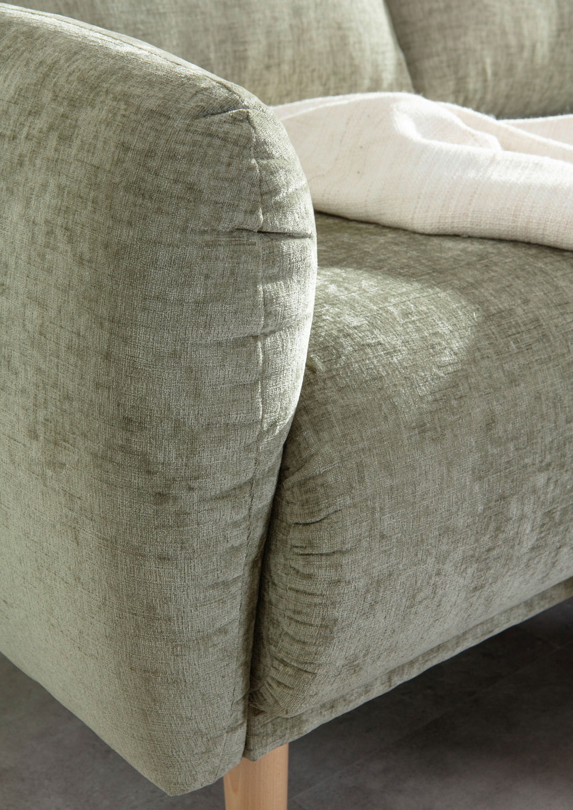 Nahaufnahme einer grünen Sofaecke mit weicher Polsterung und Holzbeinen, von der Seite betrachtet.