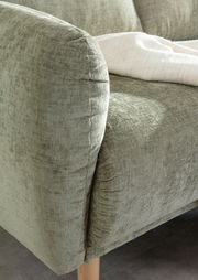 Nahaufnahme einer grünen Sofaecke mit weicher Polsterung und Holzbeinen, von der Seite betrachtet.