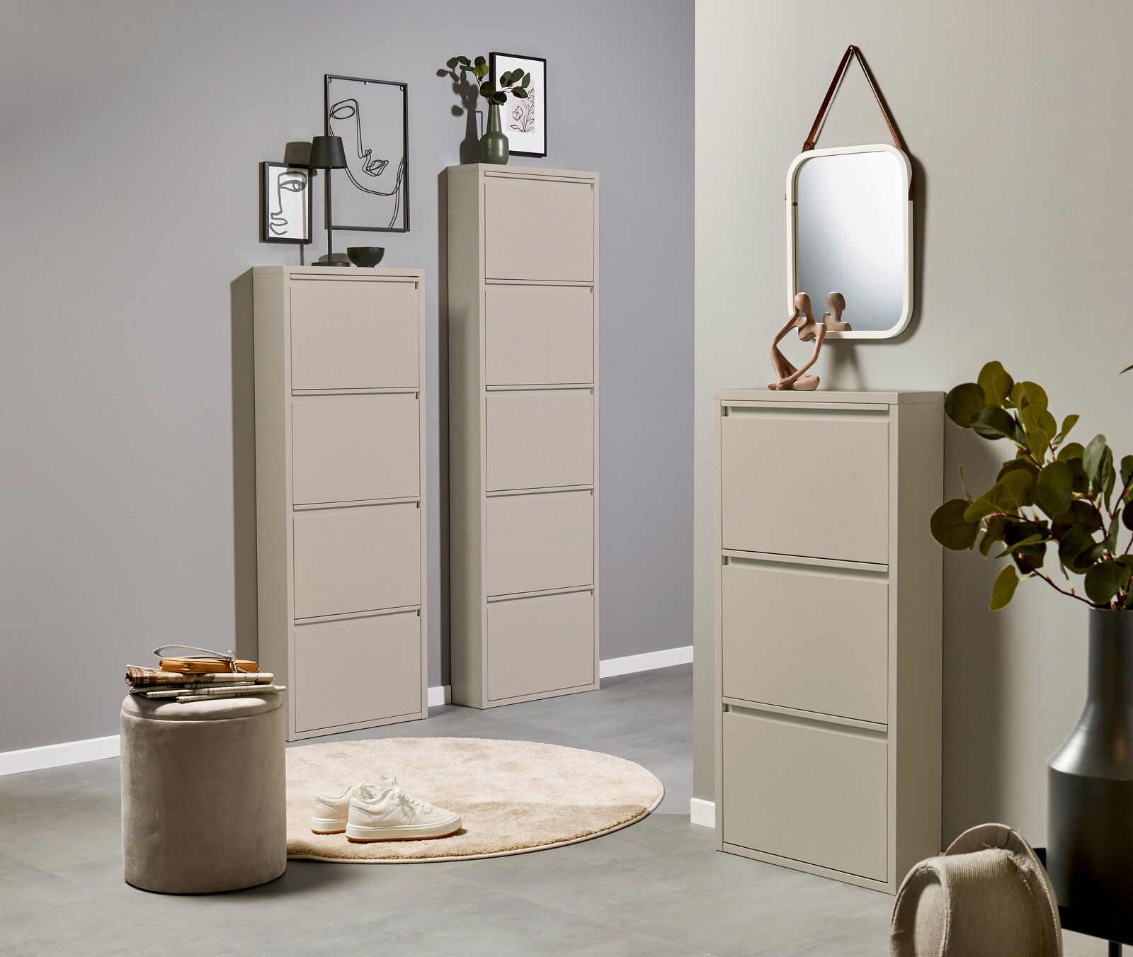 Modernes, hellbeiges Schuhschrank-Set im Flur: zwei hohe, schmale Klappschränke und ein niedrigerer Klappschrank mit Spiegel darüber, fotografiert in leichter Schrägansicht von vorn.