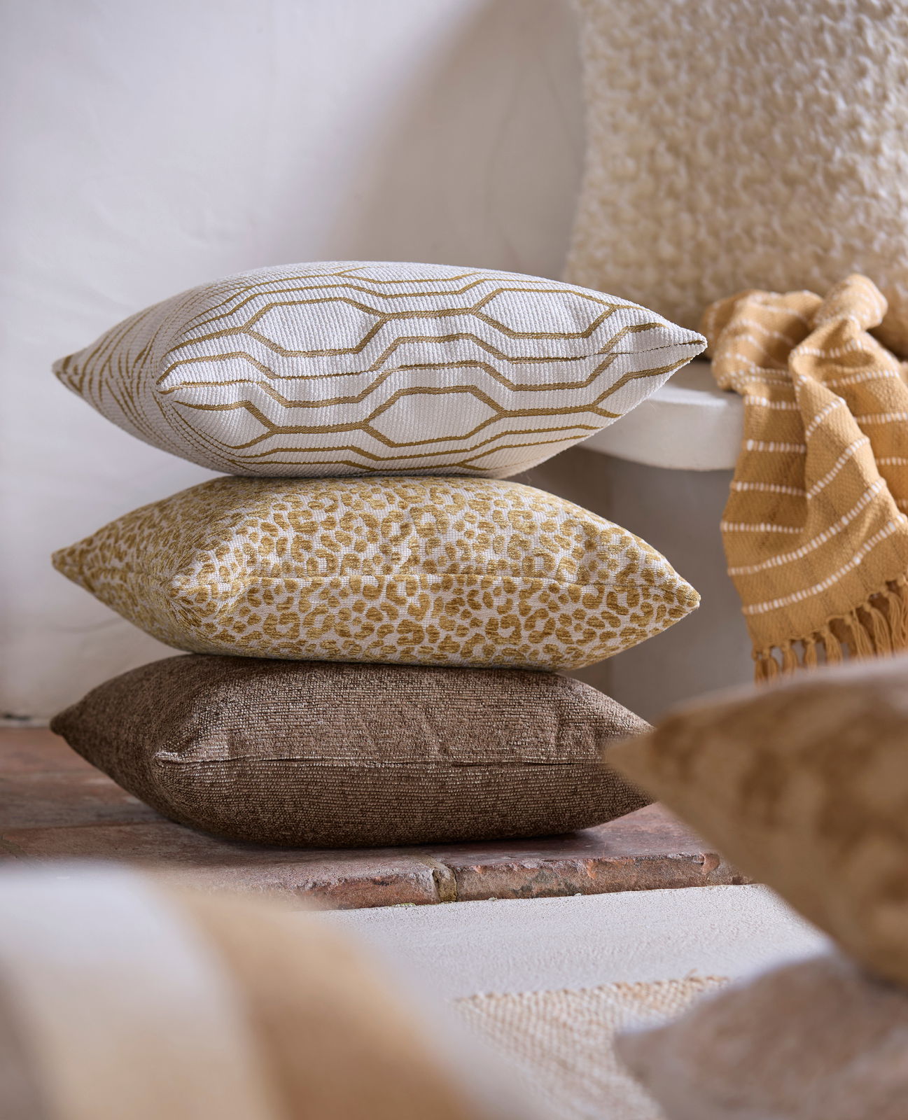 Light&Living Kissen ELYRIA Drei dekorative Kissen in verschiedenen Mustern und Farben, gestapelt auf einem Boden, seitliche Perspektive.