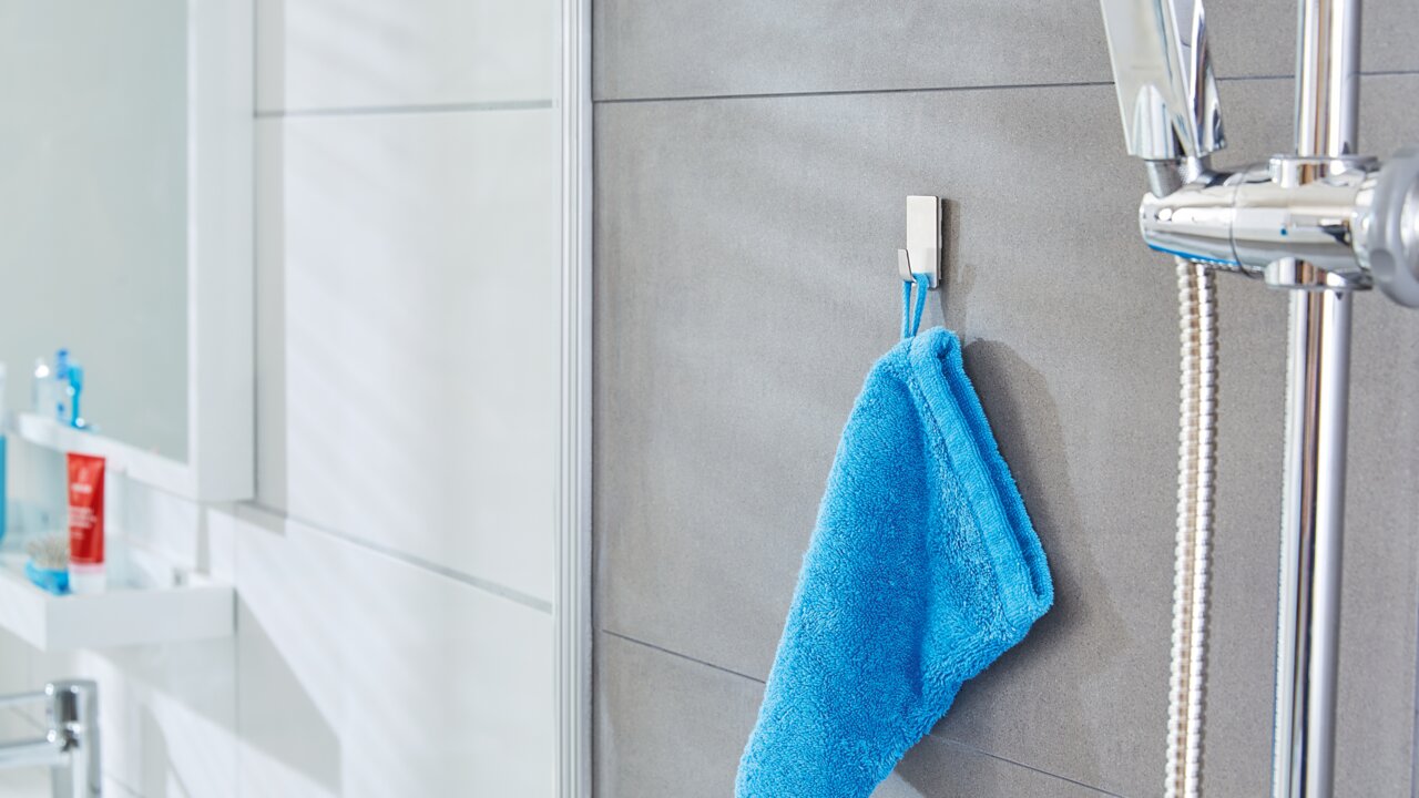 Tesa Powerstrips 2-tlg. WATERPROOF Badezimmeransicht mit einem blauen Handtuch, das an einem tesa Powerstrip Waterproof Haken an der Wand hängt.