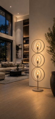 Moderne metalen vloerlamp met drie warmgloeiende lichtbronnen in decoratieve dubbele ringen, vanuit schuin vooraanzicht in een stijlvolle woonkamer