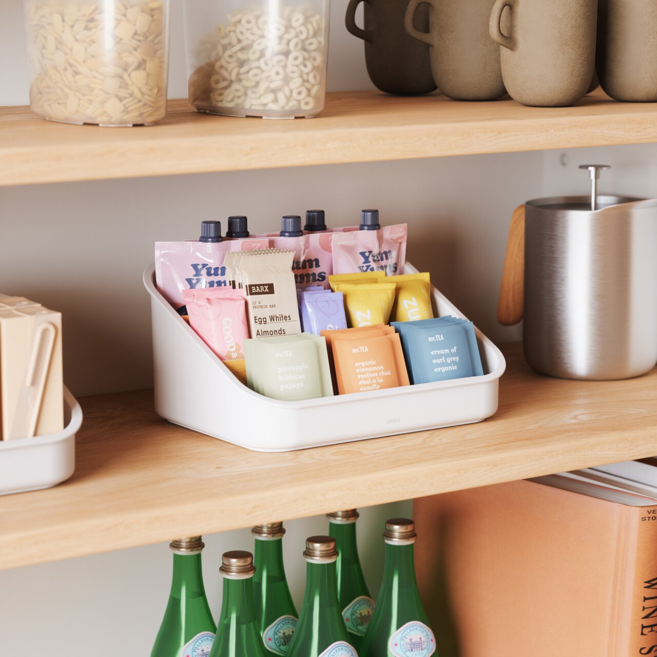 Ein weißer Organizer auf einem Holzregal, gefüllt mit verschiedenen Snacks und Teebeuteln, aus einer seitlichen Perspektive fotografiert.