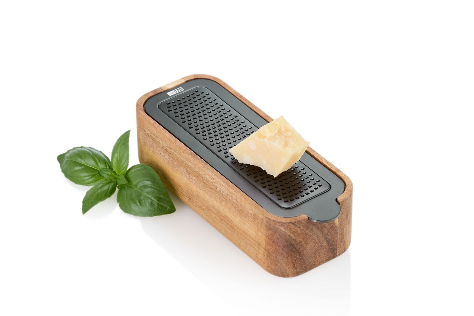 Tisch-Feinreibe CutnServe aus Holz mit einer Käsereibe und einem Stück Käse darauf, seitliche Perspektive, mit Basilikumblättern daneben.