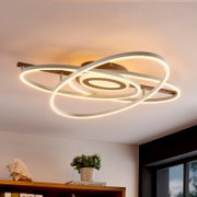 Moderne LED plafondlamp met overlappende ringen in wit met warmwit licht, aan het plafond gemonteerd, gefotografeerd vanuit een lage hoek (onderaanzicht) in een woonkamer.