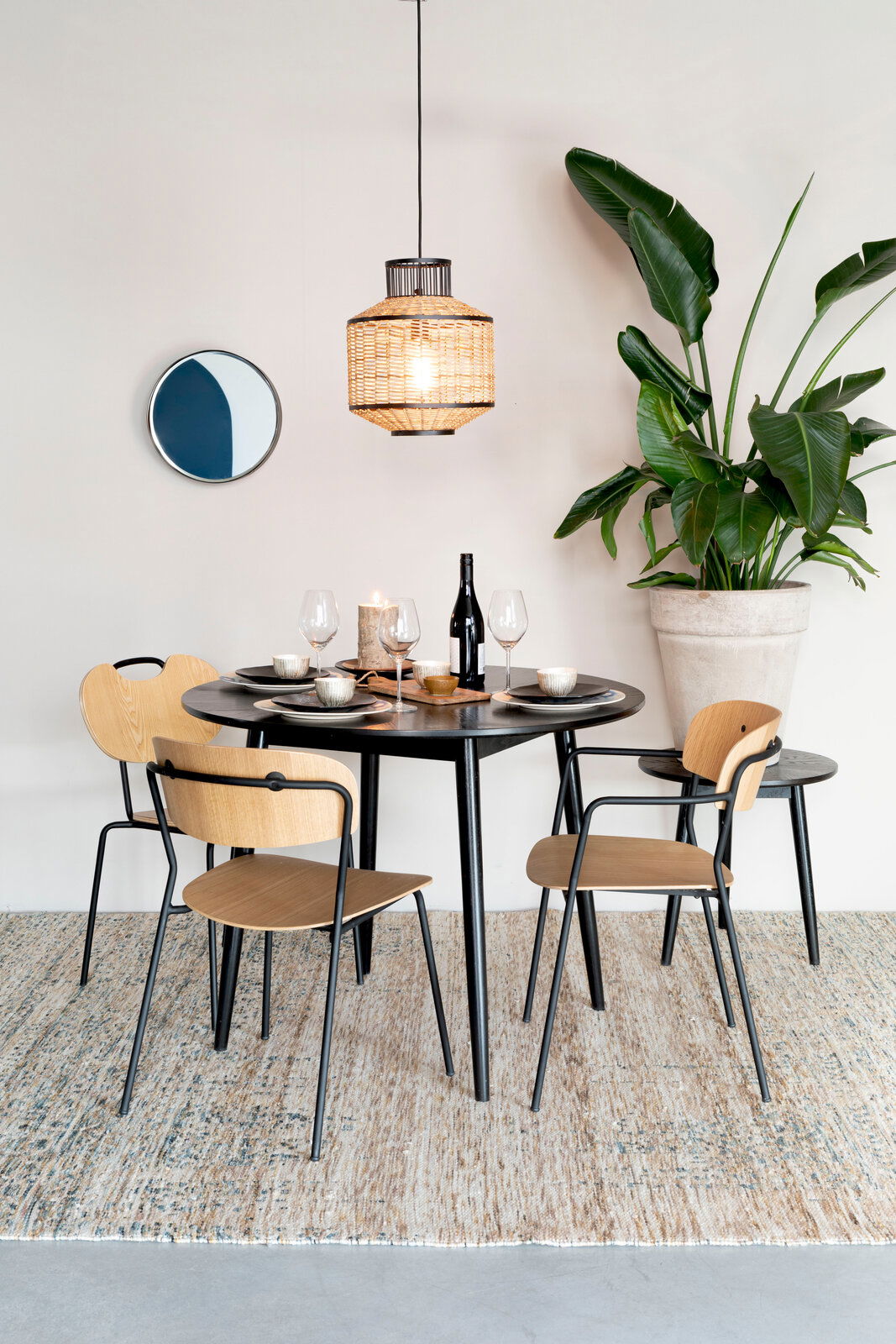 Moderner Esstisch FABIO mit schwarzer Tischplatte und Holzstühlen, dekoriert mit Geschirr und Weingläsern, aus der Perspektive von vorne betrachtet.
