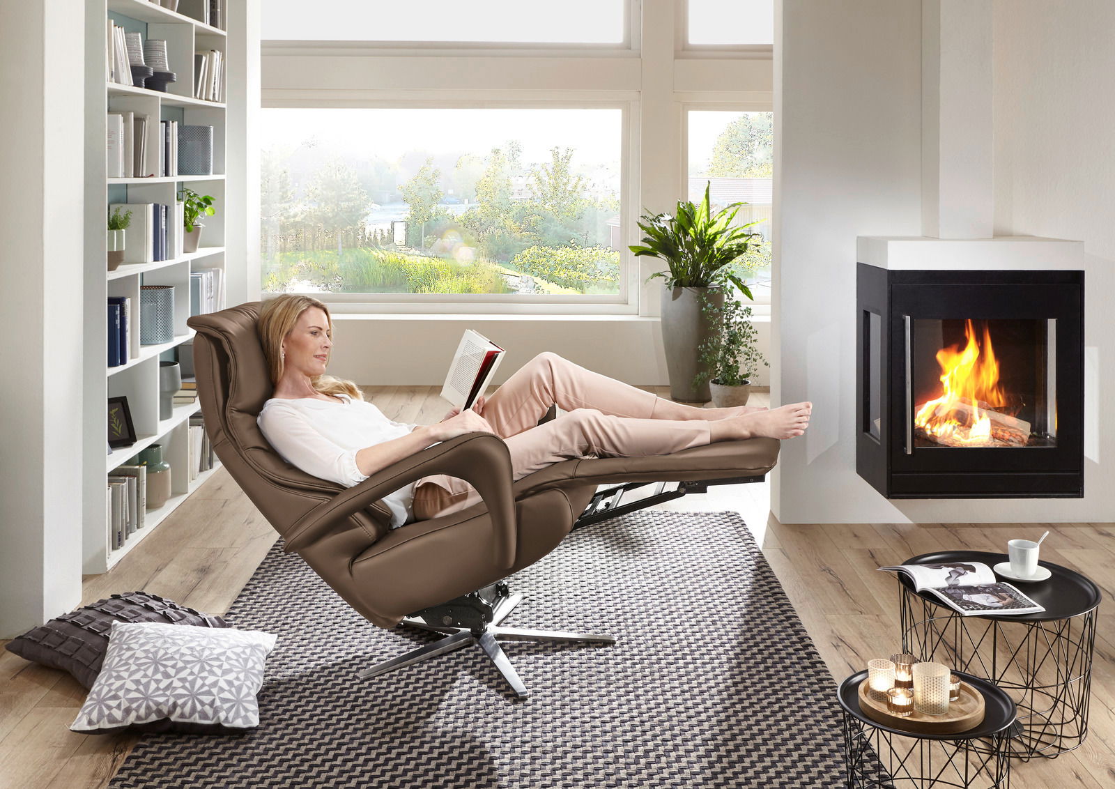 Frau entspannt in einem braunen Relax-Sessel vor einem Kamin, seitliche Perspektive