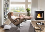 Frau entspannt in einem braunen Relax-Sessel vor einem Kamin, seitliche Perspektive
