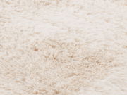 Nahaufnahme eines weichen, flauschigen Fellteppichs in cremeweißer Farbe, von oben betrachtet.