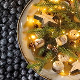 Vogelperspektive auf eine dekorative Schale mit LED-Lichterkette, Tannenzweigen, Holzsternen und kleinen Zapfen.