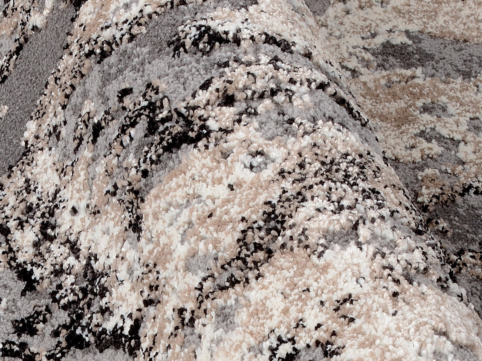 Nahaufnahme eines Designer Teppichs mit abstraktem Muster in Grau-, Beige- und Schwarztönen, aus seitlicher Perspektive fotografiert.