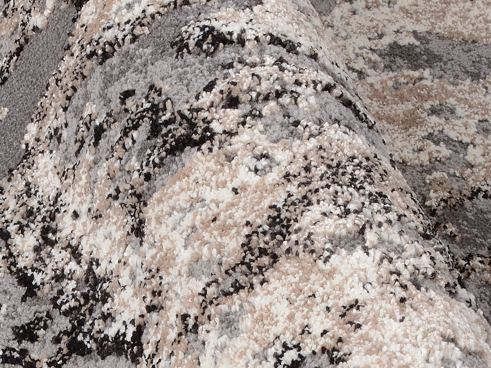 Nahaufnahme eines Designer Teppichs mit abstraktem Muster in Grau-, Beige- und Schwarztönen, aus seitlicher Perspektive fotografiert.