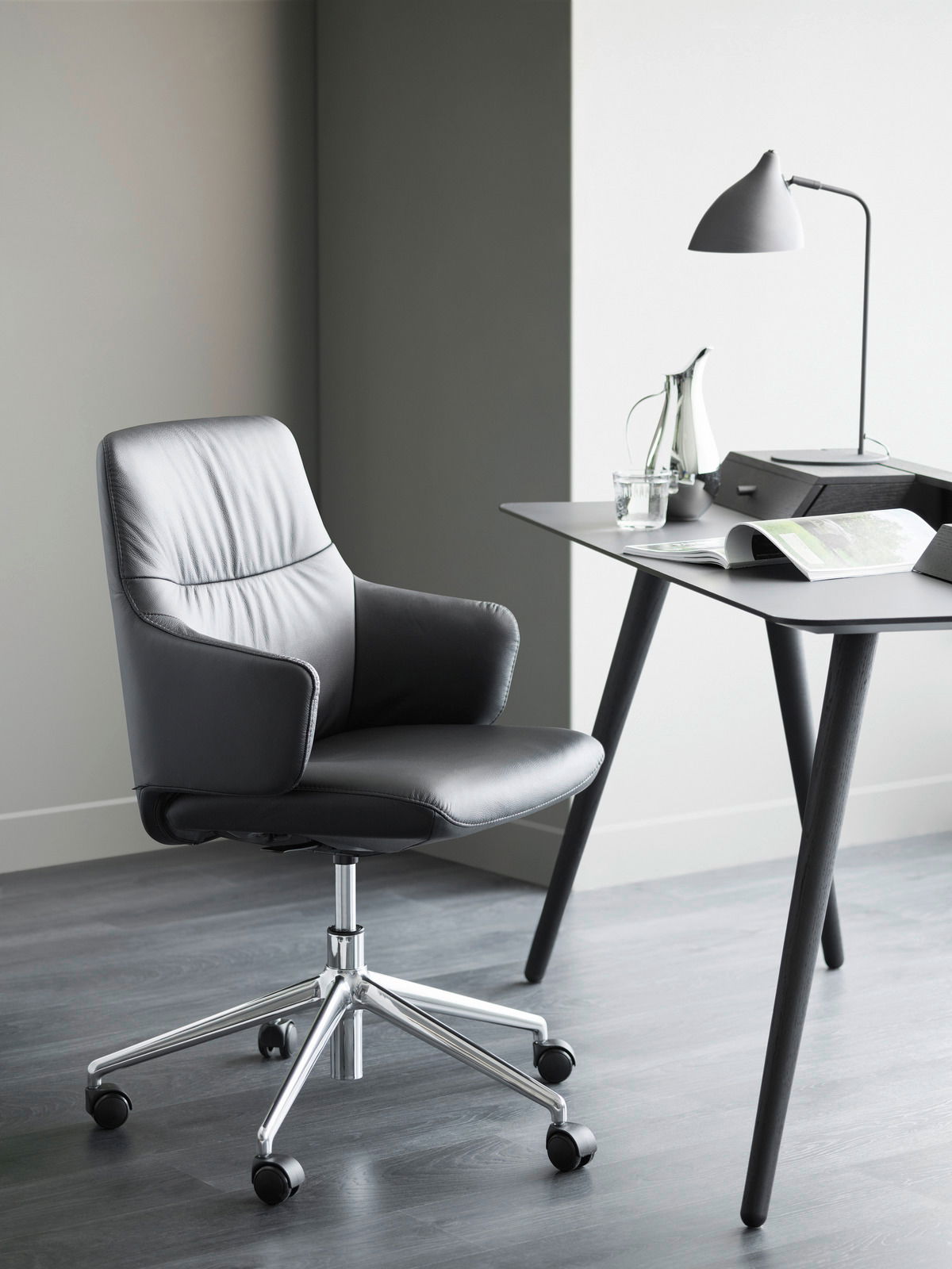 Moderner schwarzer Drehstuhl mit Armlehnen und verchromtem Fußkreuz, seitliche Perspektive.