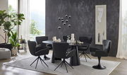 Moderner Essbereich mit rundem, schwarzem Esstisch und sechs schwarzen Armlehnstühlen auf einem hellen Teppich. Die Perspektive zeigt den Raum von der Seite mit Blick auf eine große Fensterfront und dekorative Elemente.