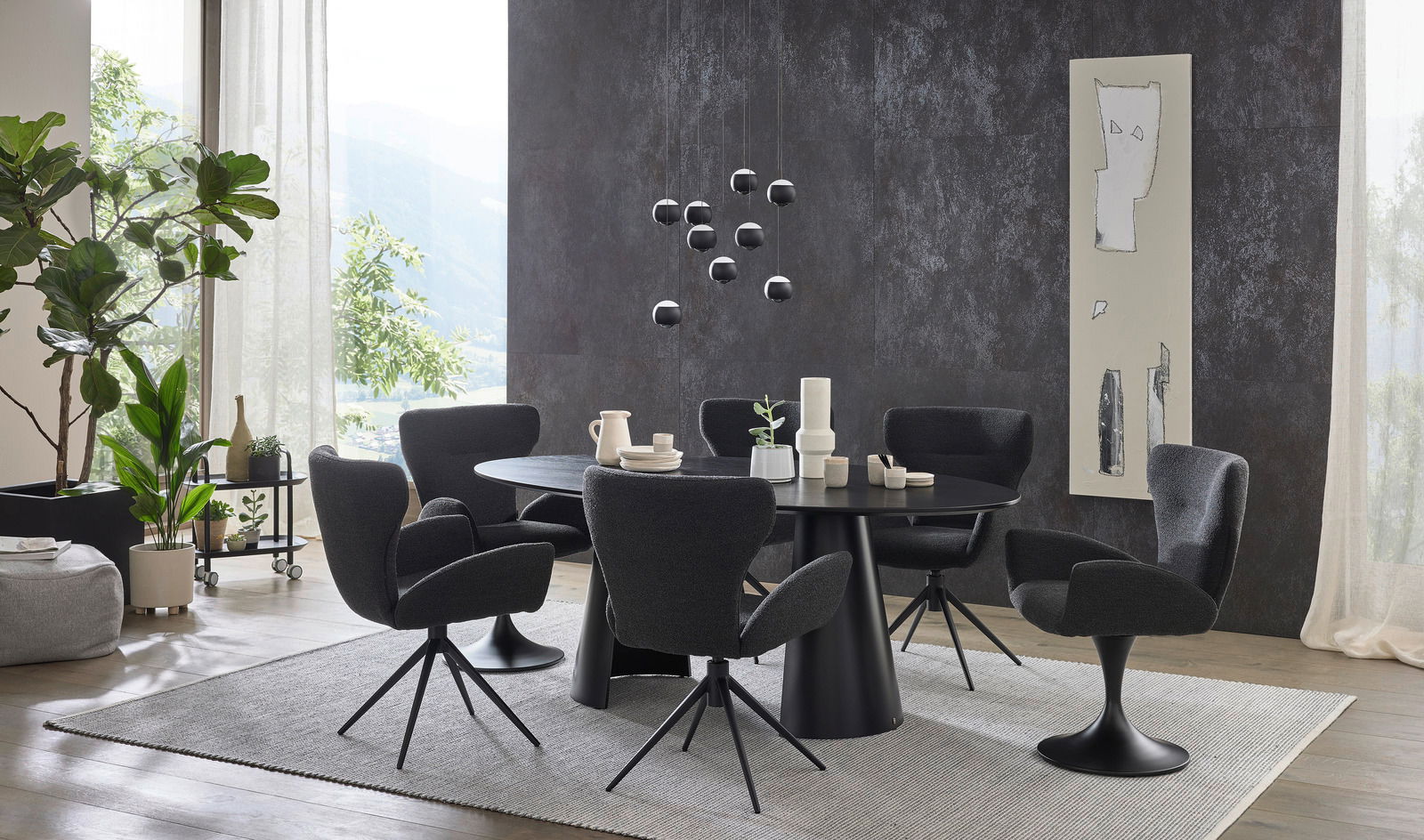 Moderner Essbereich mit rundem, schwarzem Esstisch und sechs schwarzen Armlehnstühlen auf einem hellen Teppich. Die Perspektive zeigt den Raum von der Seite mit Blick auf eine große Fensterfront und dekorative Elemente.