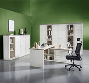 Moderne Büromöbelkombination mit weißem Eckschreibtisch, Drehstuhl und mehreren Aktenschränken in einem stilvollen Raum mit grüner Wand. Perspektive: Frontalansicht.