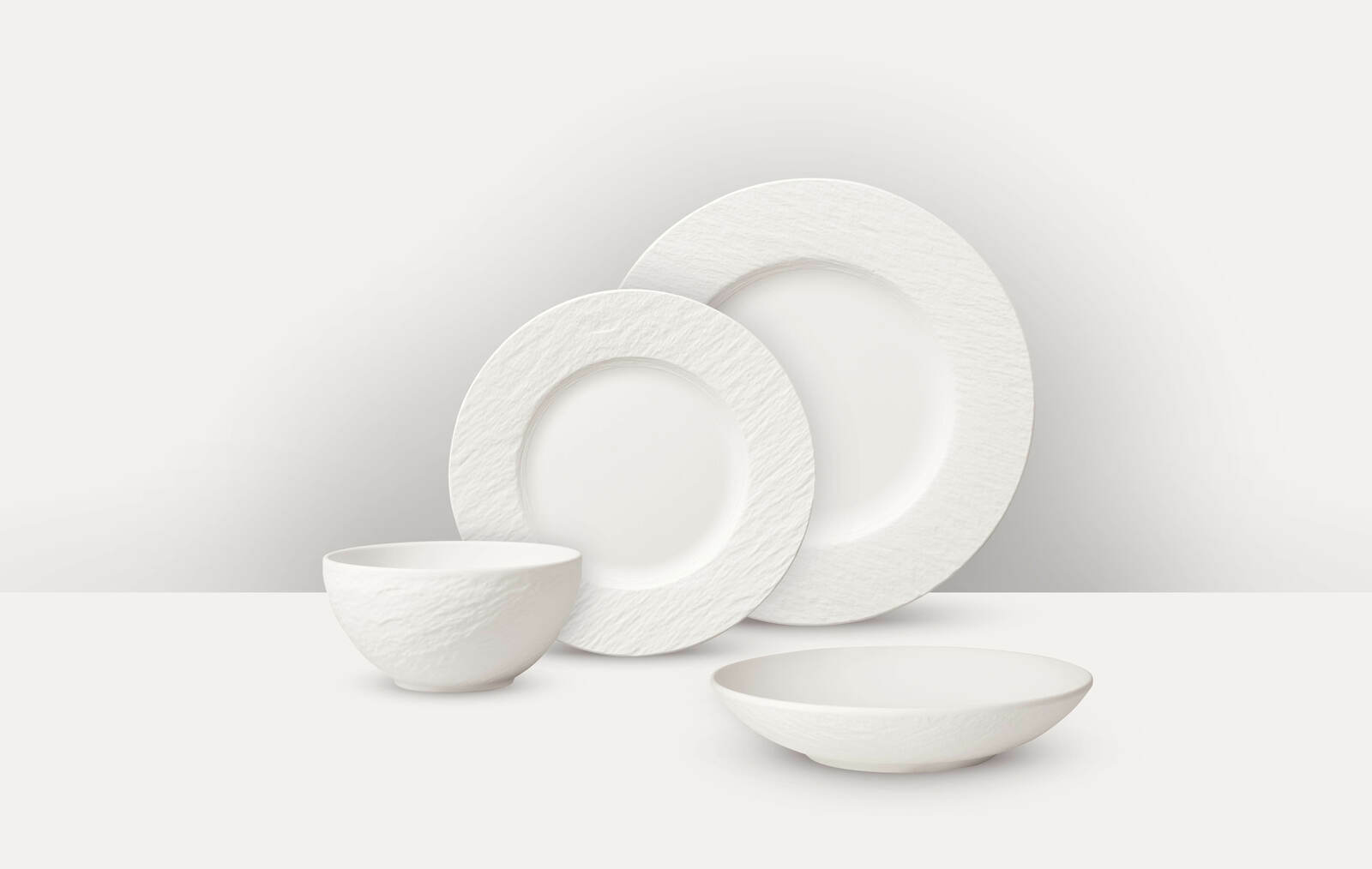 Villeroy & Boch Tafelservice 16-tlg. MANUFACTURE ROCK BLANC Weißes Tafelservice 16-tlg. mit strukturiertem Rand, bestehend aus zwei Tellern, einer Schale und einem tiefen Teller, aus seitlicher Perspektive fotografiert.
