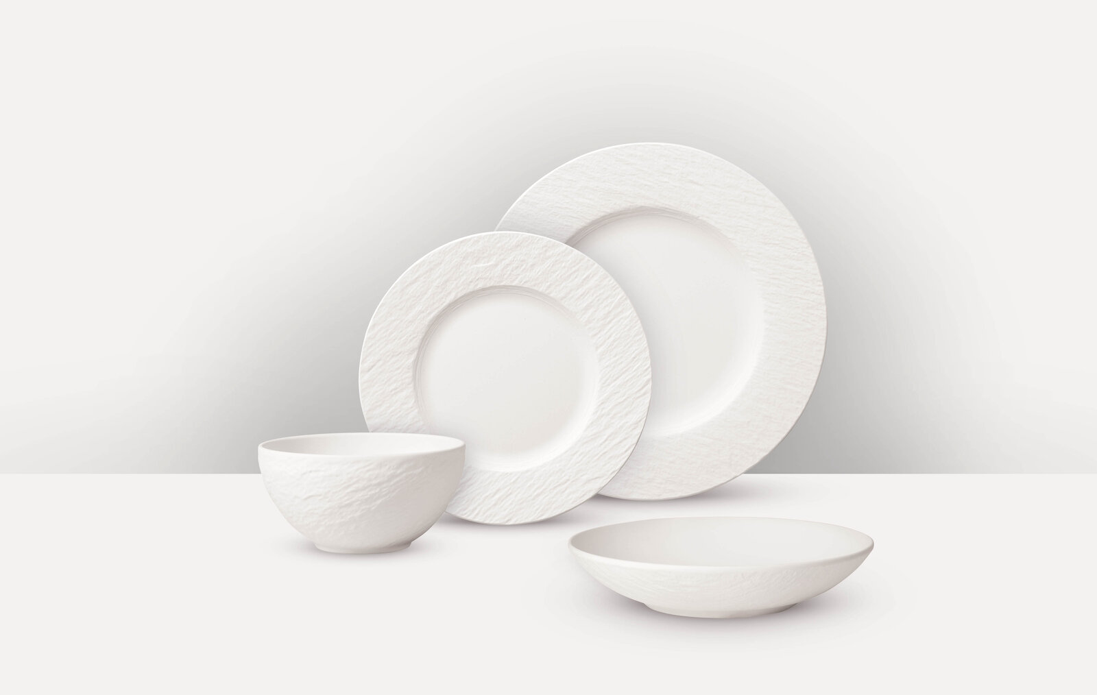 Villeroy & Boch Tafelservice 16-tlg. MANUFACTURE ROCK BLANC Weißes Tafelservice 16-tlg. mit strukturiertem Rand, bestehend aus zwei Tellern, einer Schale und einem tiefen Teller, aus seitlicher Perspektive fotografiert.
