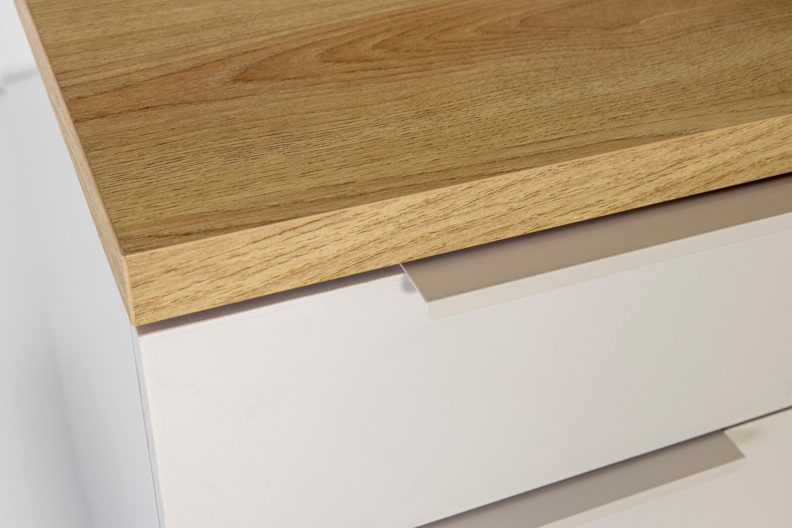 Detailaufnahme einer modernen Kommode mit weißer Front und Holzplatte in Eichenoptik, aus schräger Perspektive von oben