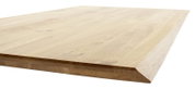 Nahaufnahme einer Tischplatte aus hellem Holz mit abgeschrägter Kante, perspektivisch von der Seite aufgenommen.