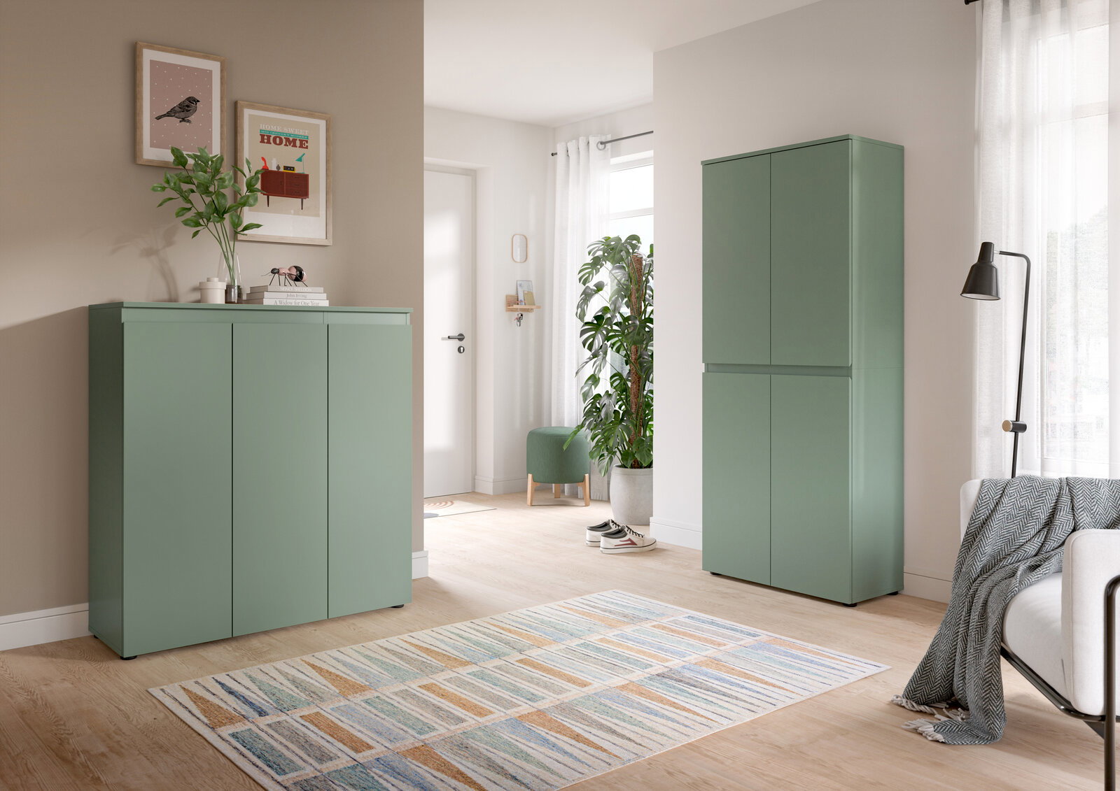 Modernes Wohnzimmer mit zwei matten, salbeigrünen Schränken (links niedriges Sideboard, rechts hoher Schrank) vor heller Wand, Perspektive: frontale Ansicht mit leichtem Weitwinkel.