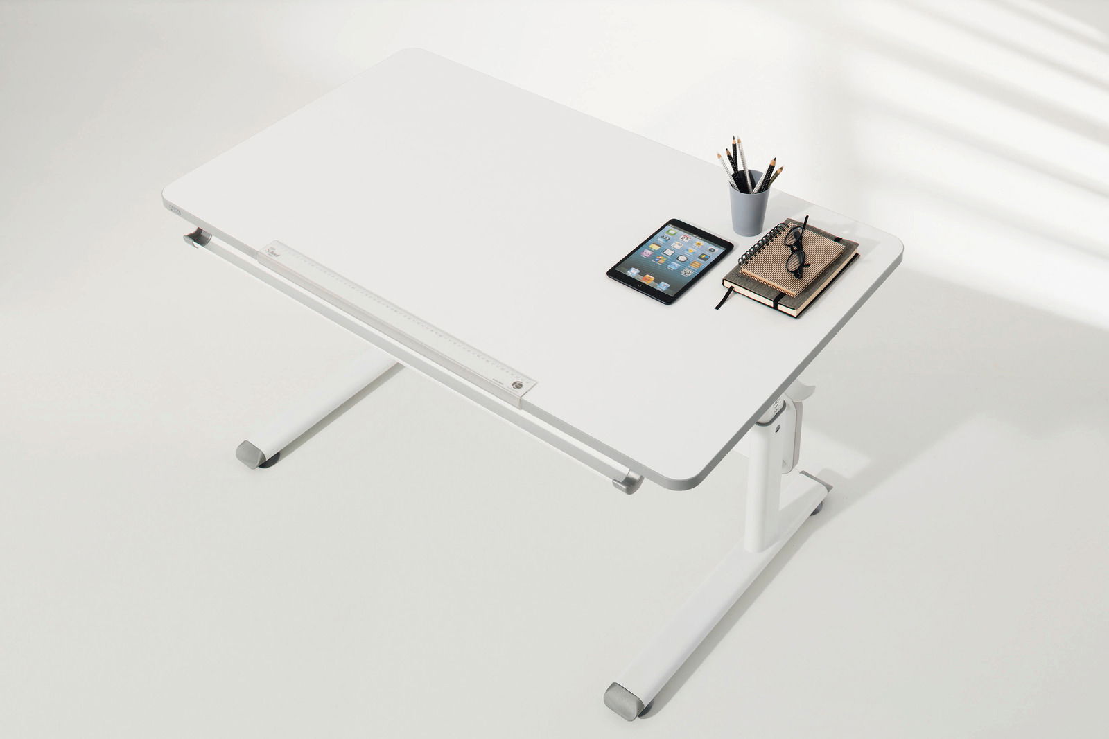 Moderner weißer Schreibtisch von oben, mit Tablet, Notizbuch, Brille und Stiftehalter.