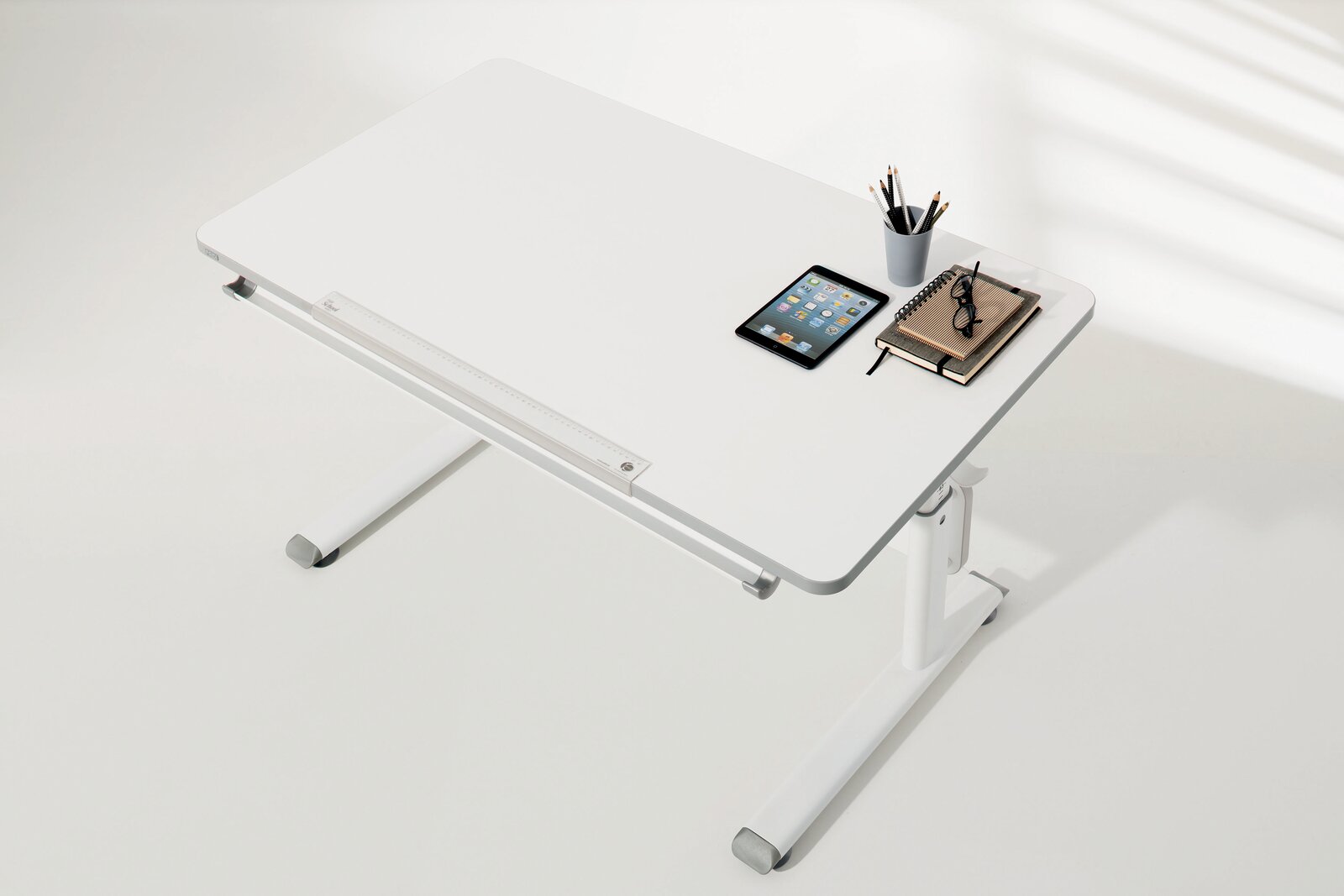 Moderner weißer Schreibtisch von oben, mit Tablet, Notizbuch, Brille und Stiftehalter.