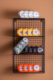 Verschiedene Tischuhren mit Kalenderfunktion in bunten Farben auf einem Gitterregal, seitliche Perspektive.