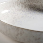 Detailaufnahme einer glasierten Keramikschale in Cremeweiß mit bläulich-grauer Sprenkelung, aus schräger Nahperspektive von oben in die Schale fotografiert