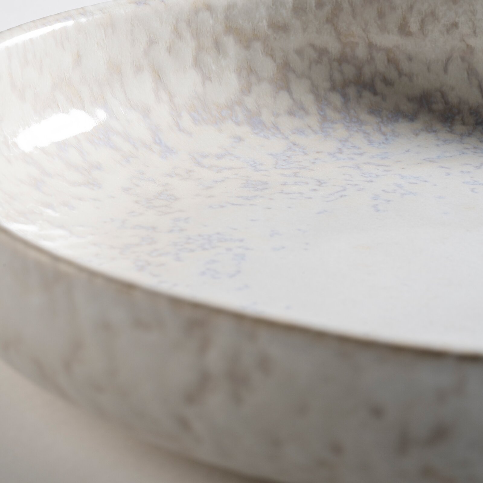 Detailaufnahme einer glasierten Keramikschale in Cremeweiß mit bläulich-grauer Sprenkelung, aus schräger Nahperspektive von oben in die Schale fotografiert