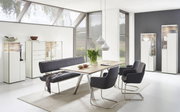 Moderne eettafel met houten blad en metalen poten, omringd door stijlvolle stoelen en een bank, in een lichte, elegante ruimte met grote ramen. Perspectief: vooraanzicht.