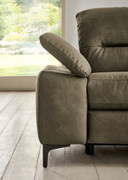 Nahaufnahme eines modernen Longchairs in Olivgrün mit verstellbarer Armlehne, seitliche Perspektive, im Hintergrund ein Fenster mit Blick ins Grüne.