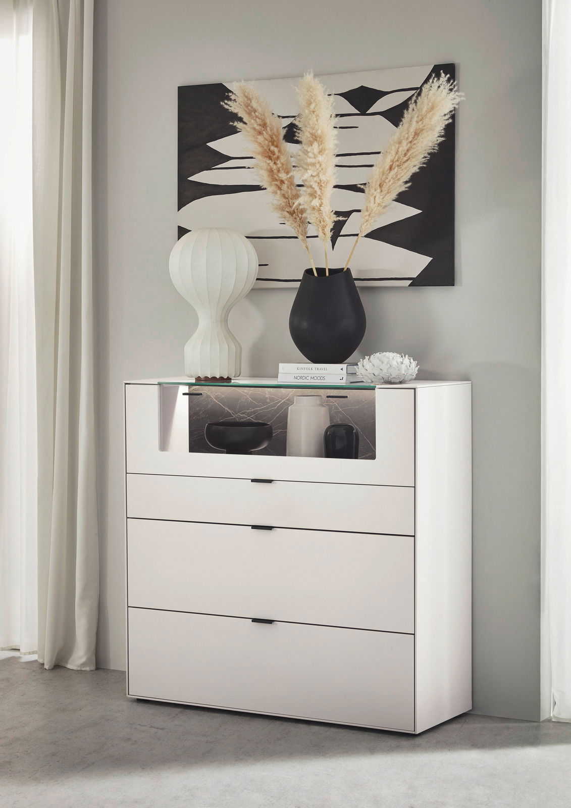 Dieter Knoll Highboard MONTESA Frontale Ansicht eines modernen weißen Highboards mit drei Schubladen und einem offenen Fach, dekoriert mit einer Vase und Büchern.