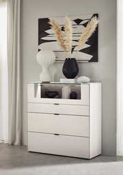 Frontale Ansicht eines modernen weißen Highboards mit drei Schubladen und einem offenen Fach, dekoriert mit einer Vase und Büchern.