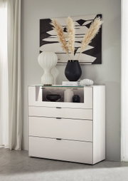 Frontale Ansicht eines modernen weißen Highboards mit drei Schubladen und einem offenen Fach, dekoriert mit einer Vase und Büchern.