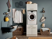 Moderner Hauswirtschaftsraum mit Waschmaschine in einem Hochschrank integriert, umgeben von Körben und Hängeregalen, aus der Frontalperspektive.