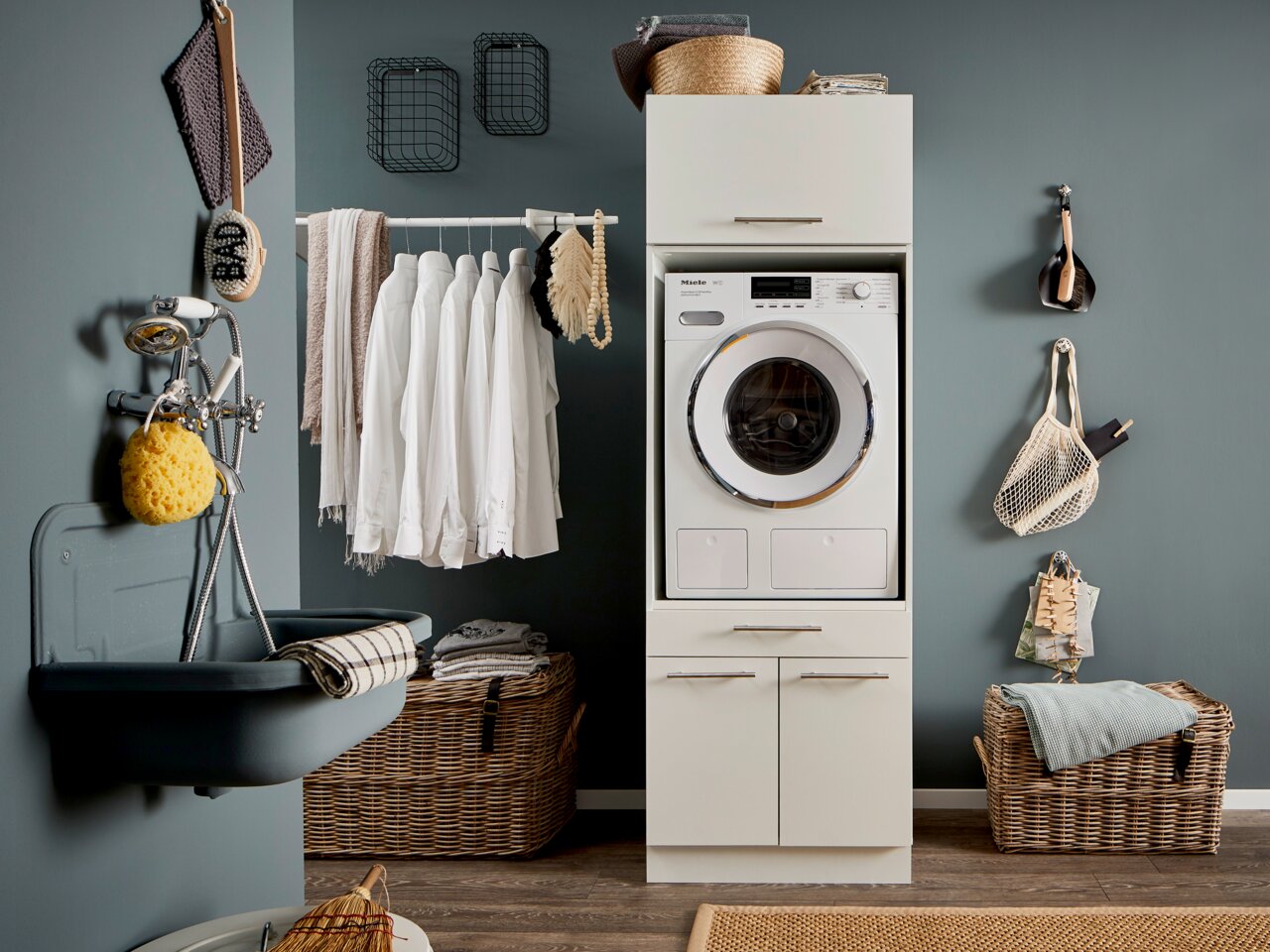 Moderne bijkeuken met een in een hoge kast geïntegreerde wasmachine, omringd door manden en hangende planken, gezien vanuit een vooraanzicht.