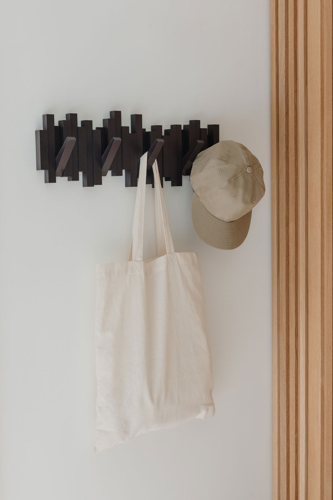 Moderne Wandgarderobe mit mehreren Haken, an der eine beige Stofftasche und eine beige Kappe hängen, seitliche Perspektive.