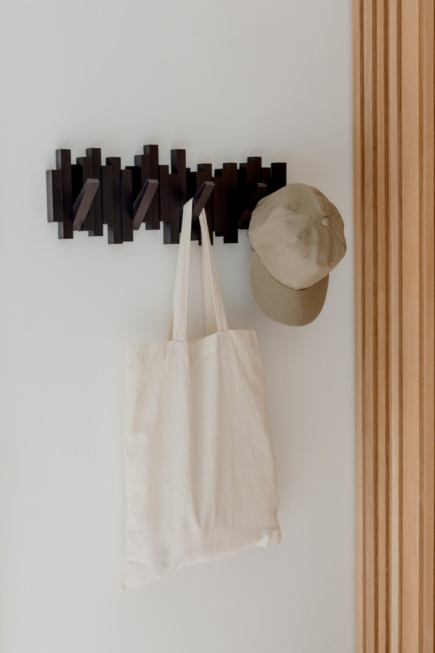 Moderne Wandgarderobe mit mehreren Haken, an der eine beige Stofftasche und eine beige Kappe hängen, seitliche Perspektive.