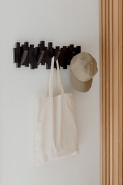 Moderne Wandgarderobe mit mehreren Haken, an der eine beige Stofftasche und eine beige Kappe hängen, seitliche Perspektive.