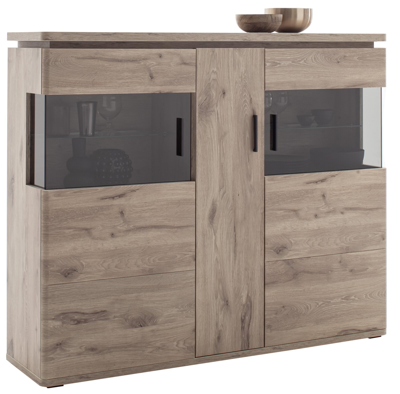 Vooraanzicht van een moderne ladekast/highboard in lichte eikenhoutlook met twee vitrinekasten van getint glas en zwarte handgrepen, op een witte achtergrond