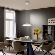 Weiße, minimalistische Pendelleuchte mit flachem Schirm über einem modernen Esstisch im Esszimmer, Seitenansicht in leichter Untersicht.
