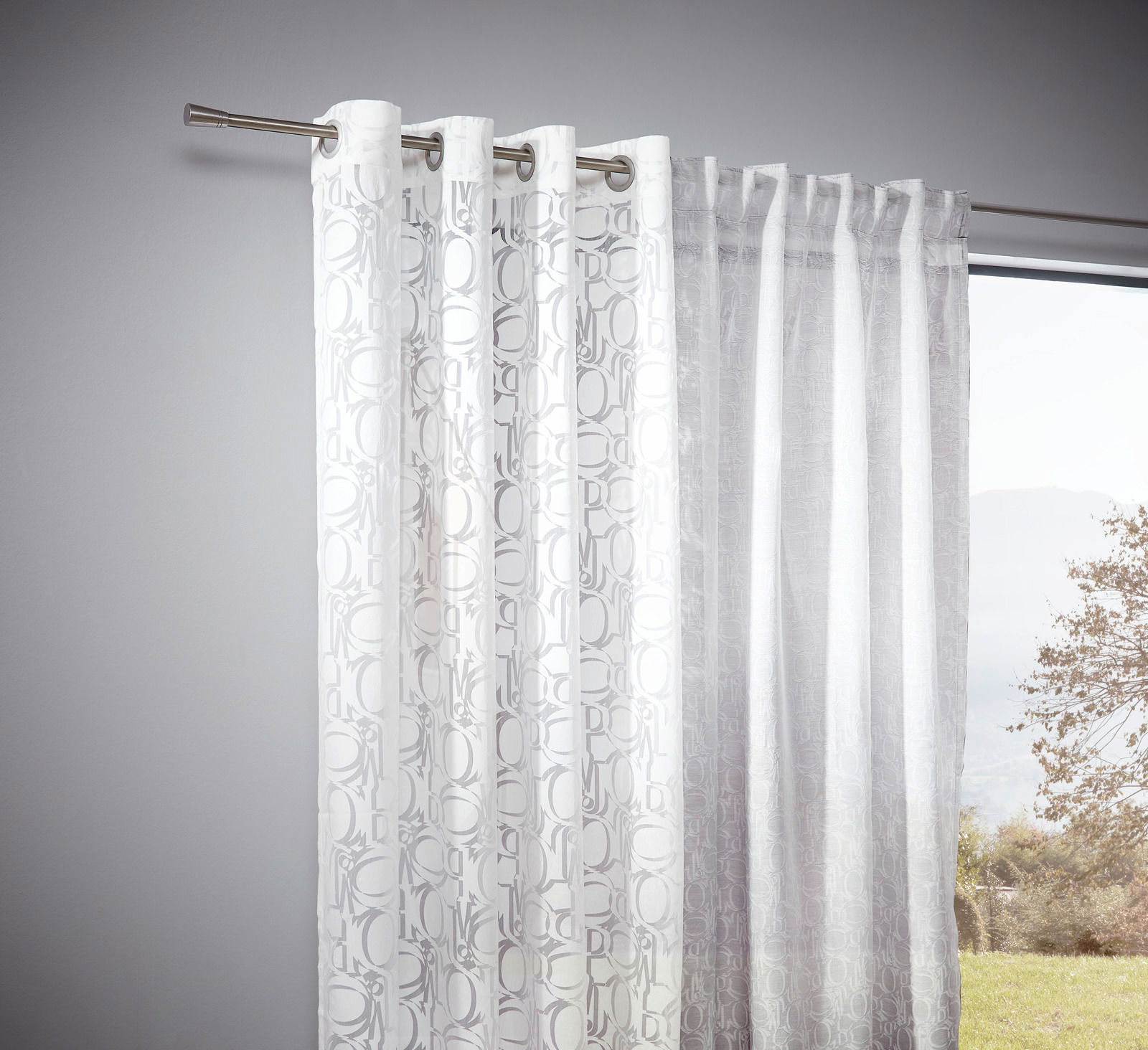 Weiße Vorhänge mit feinem Ornamentmuster, aufgehängt an einer Gardinenstange, seitliche Perspektive mit Blick nach draußen.