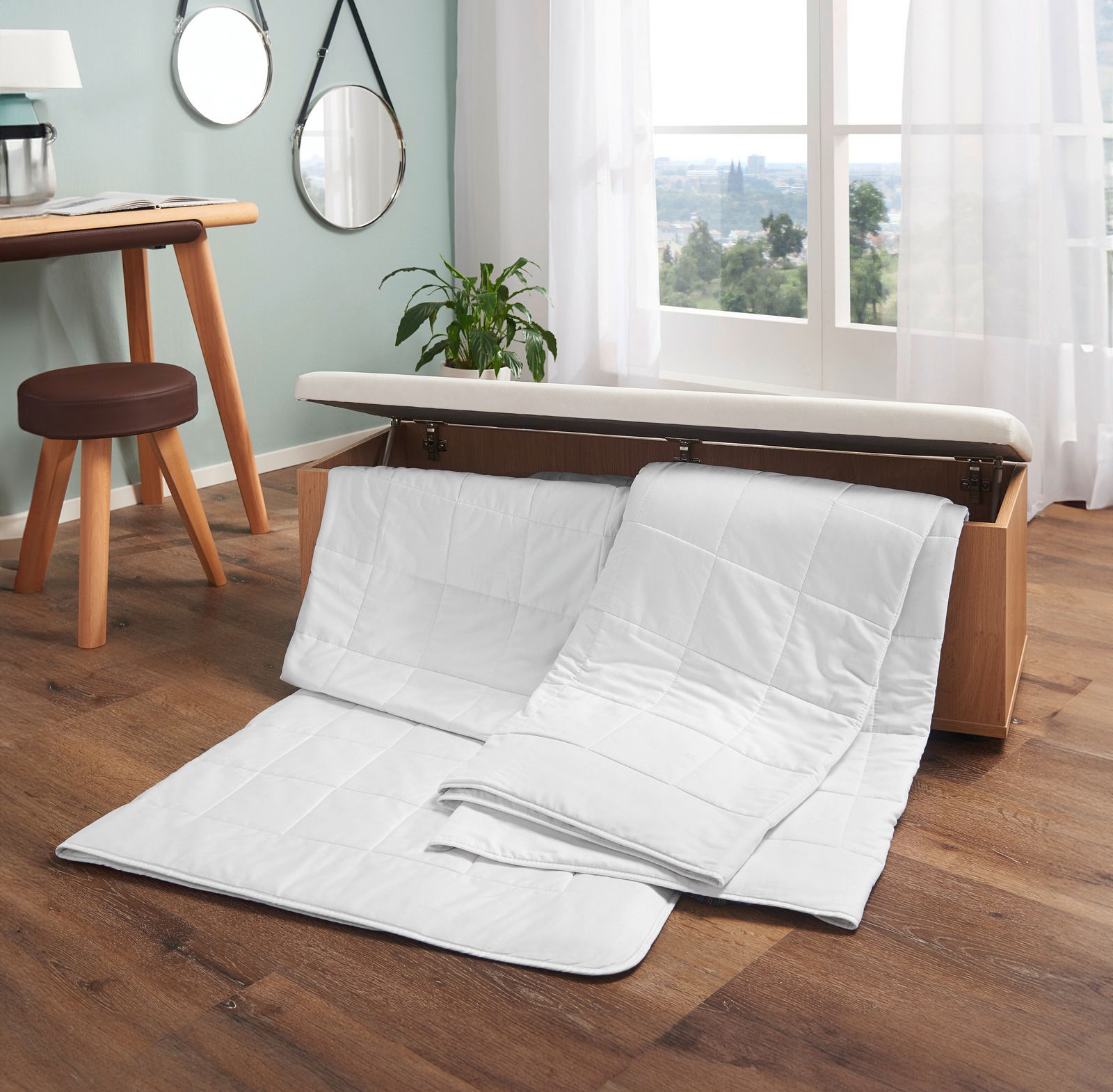 Wildseidendecke Superlight in einem modernen Raum, teilweise aus einer Holztruhe herausgezogen, mit Blick auf ein Fenster mit Vorhängen.