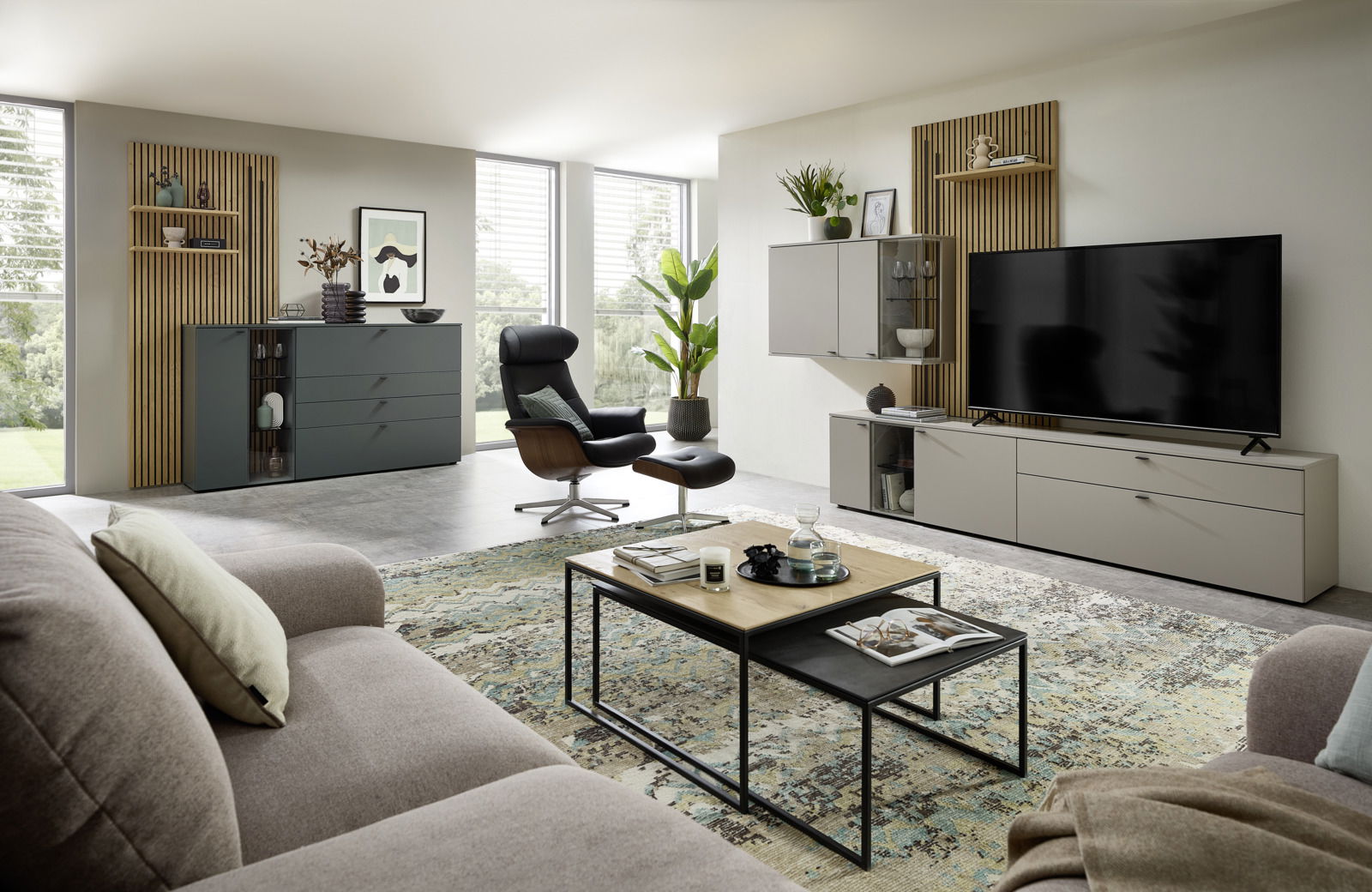Moderne Wohnzimmeransicht mit Wandkombination, bestehend aus grauen Schränken und Regalen, einem großen Fernseher, einem schwarzen Sessel und einem Couchtisch, aus der Perspektive eines gemütlichen Wohnzimmers.