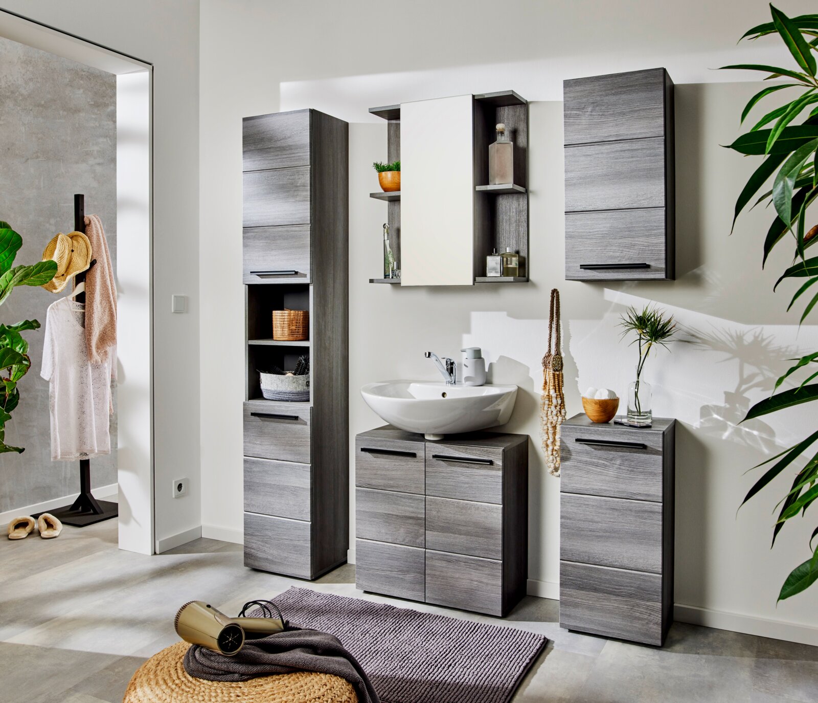 Modernes Badezimmermöbel-Set in grauer Holzoptik mit Waschbecken-Unterschrank, Hochschrank, Hängeschränken und Regal, aufgenommen in leicht schräger Frontansicht auf Augenhöhe.