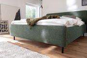 Grünes Polsterbett in einem modernen Schlafzimmer, seitliche Perspektive, mit weißer Bettwäsche und einer gemusterten Decke.